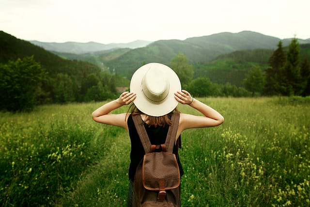 lady holding her hat while looking out to the open green field